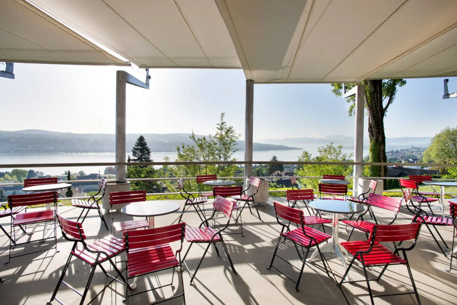Tables and red chairs on a patio overlooking lake Zurich.