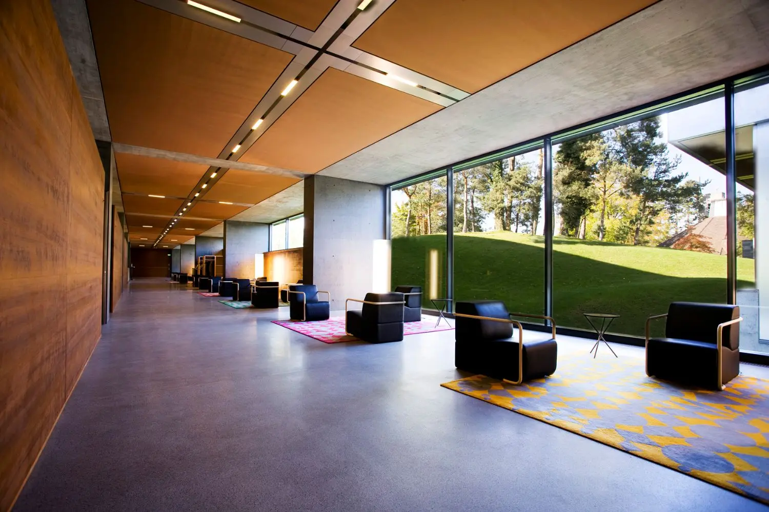 Lounge chairs and carpets along a bright hallway with glass windows.