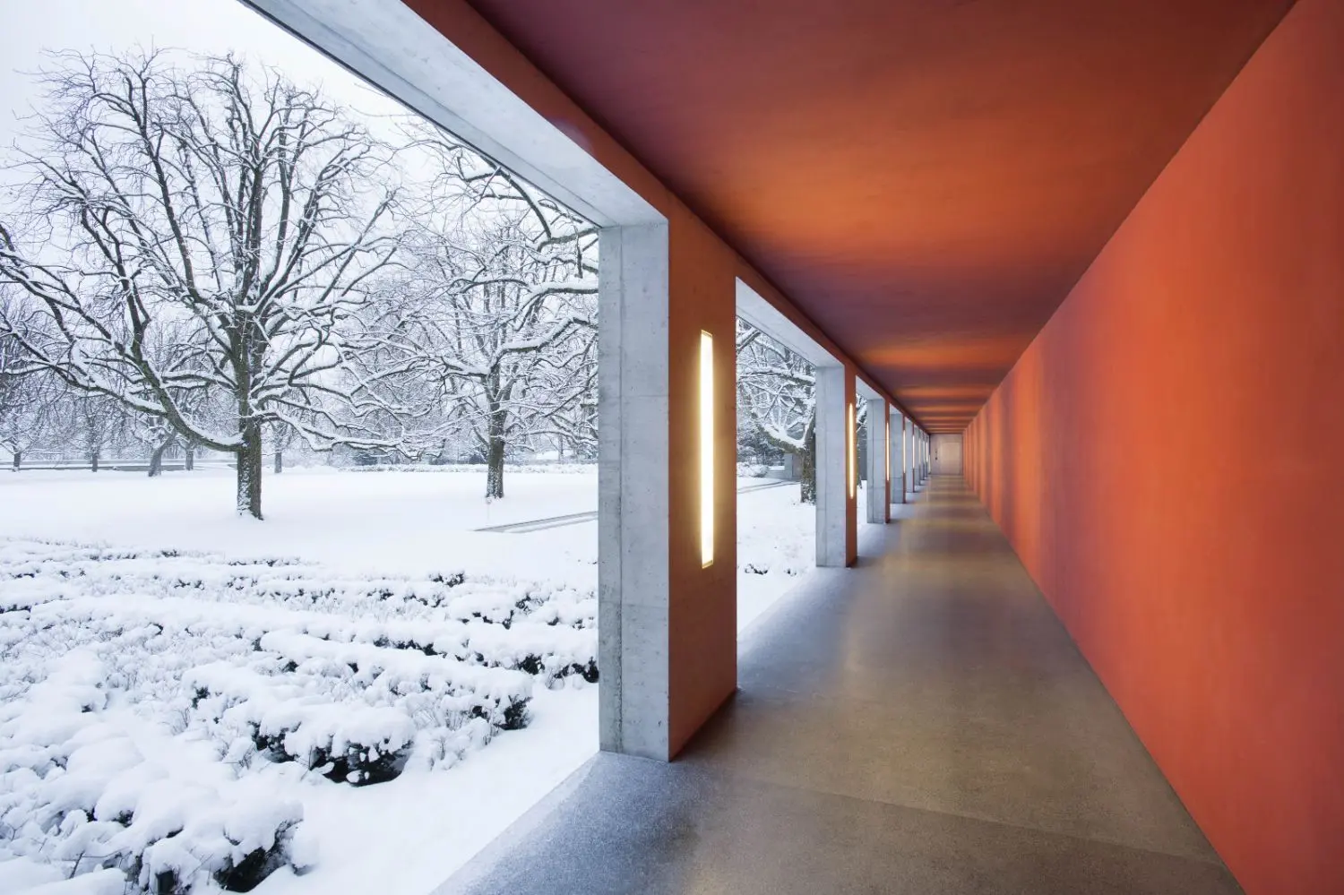 A red lit concrete corridor next to a snow covered landscape.