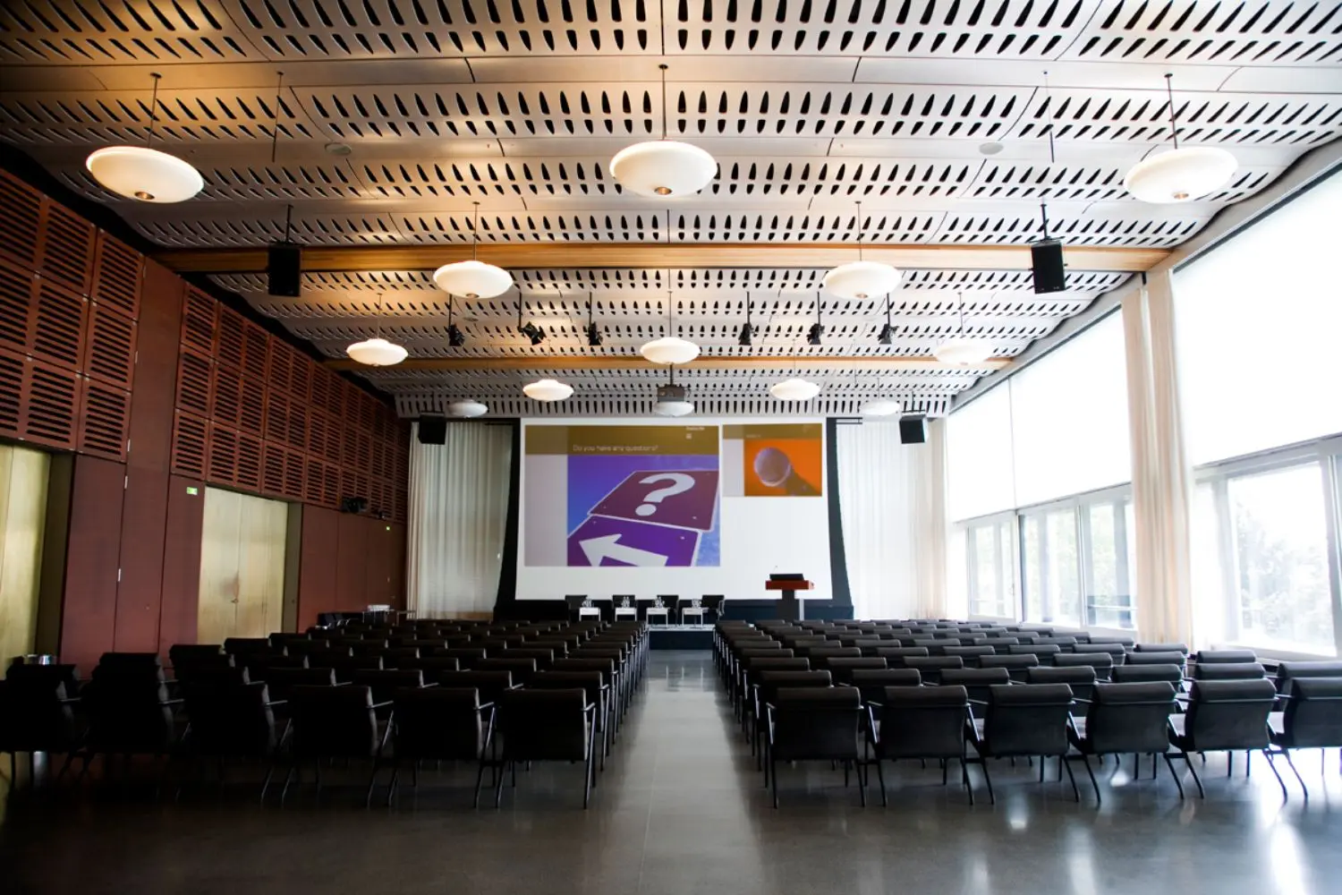 Two blocks of seats with a corridor in the middle leading to a podium with a screen.