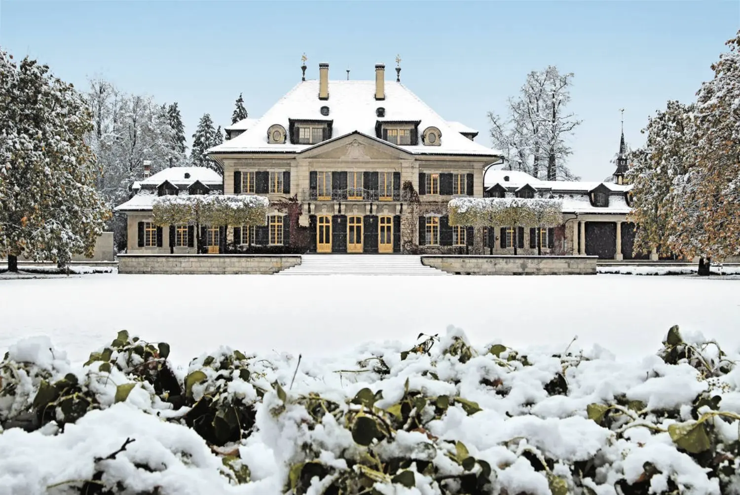 A baroque villa with a snow covered lawn and bushes in the foreground.